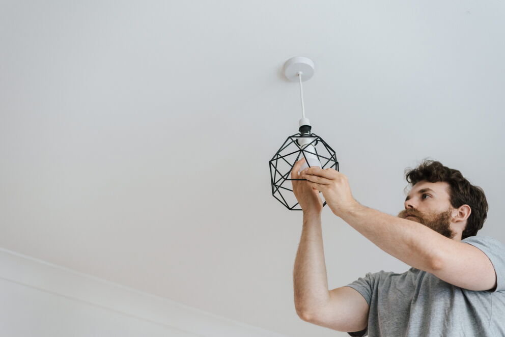 Mann mit grauem T-shirt schraubt Glühbirne an eine Lampe