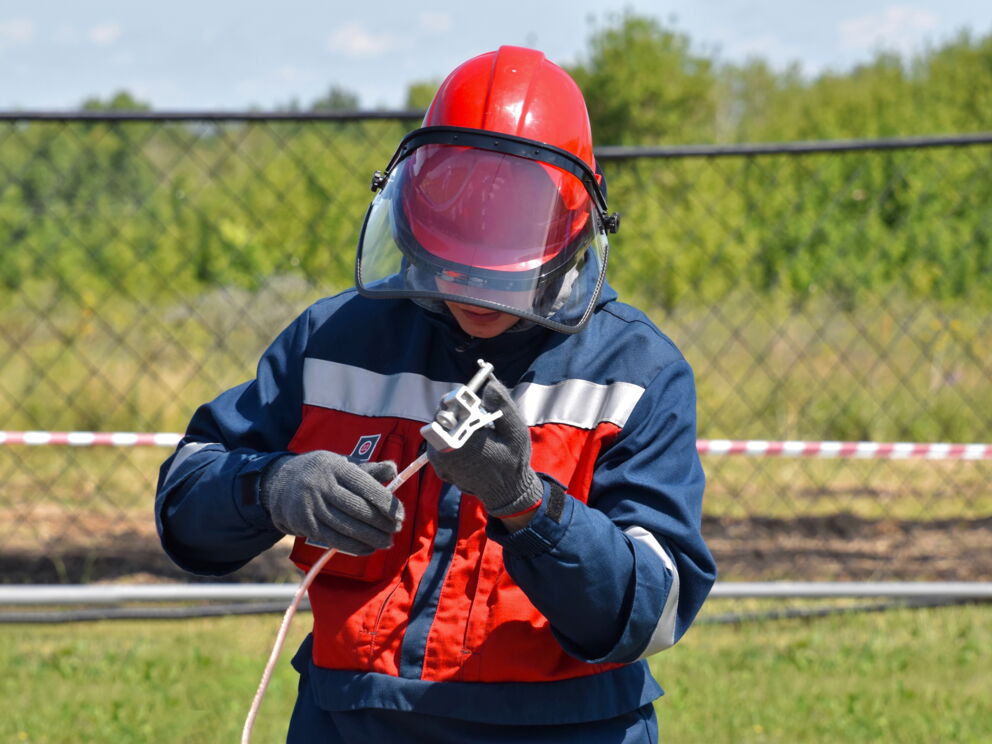 Person mit Schutzkleidung sichert ein Erdungskabel ab