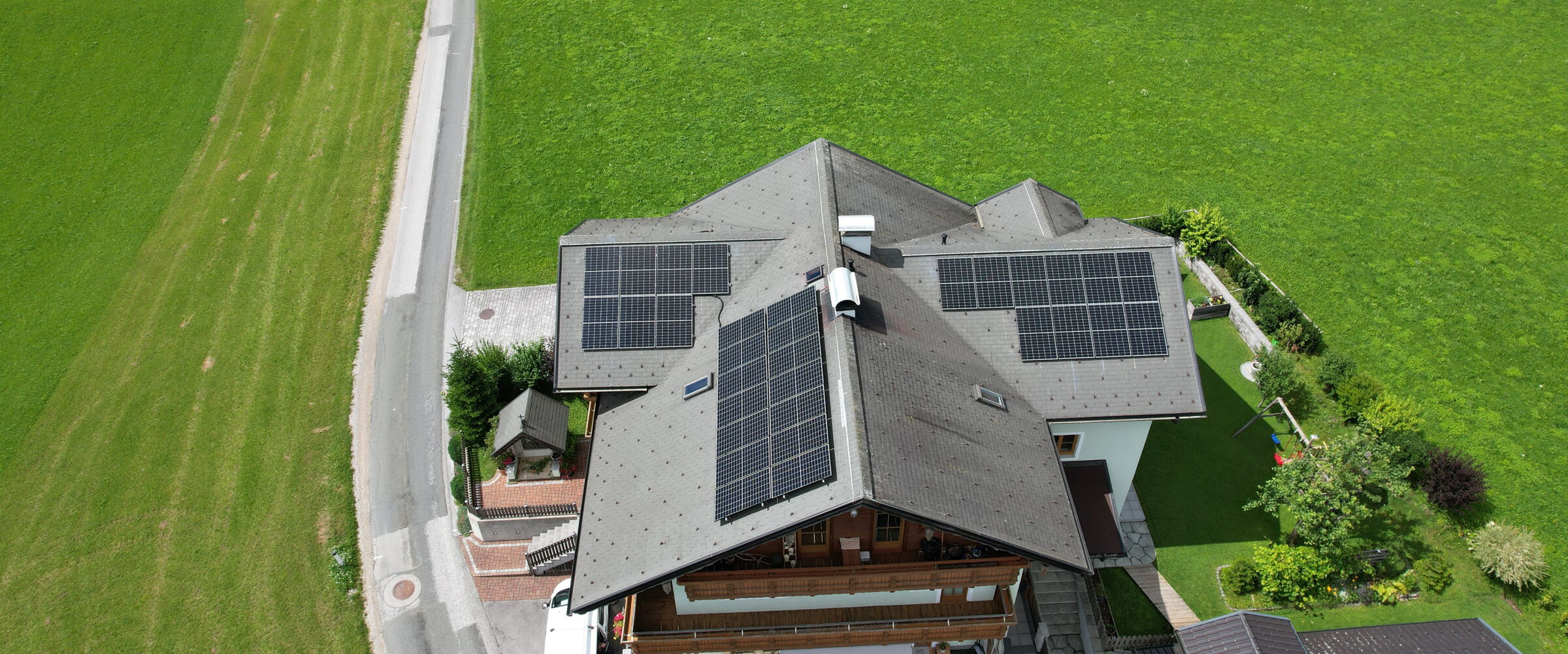 Eine Photovoltaik-Anlage auf einem Hausdach von oben mit viel Grünfläche im Hintergrund