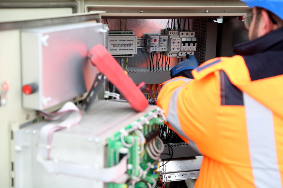 Ein Elektriker in Arbeitskleidung arbeitet an einem Sicherungskasten